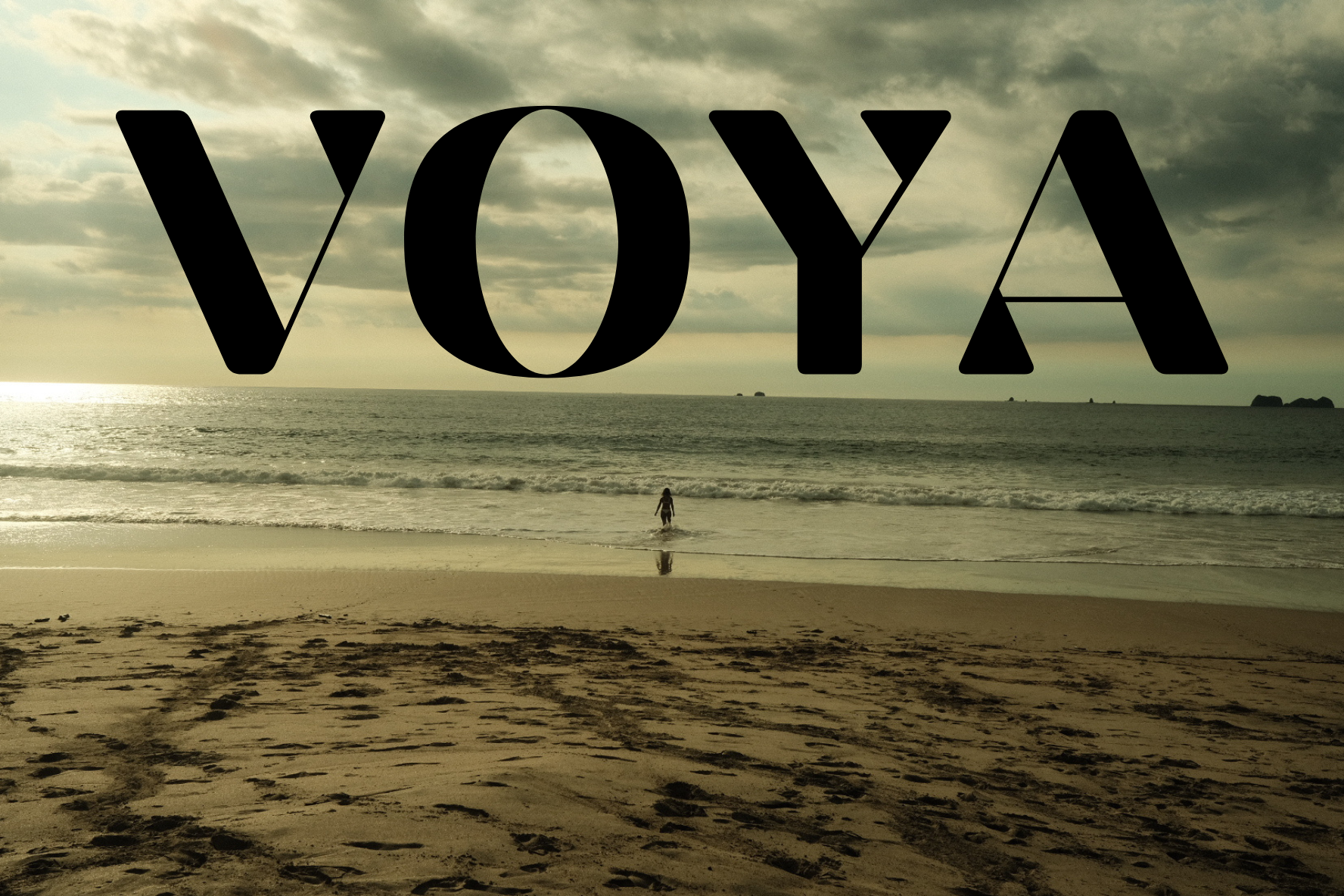VOYA sobre una playa al atardecer, con una persona entrando al océano